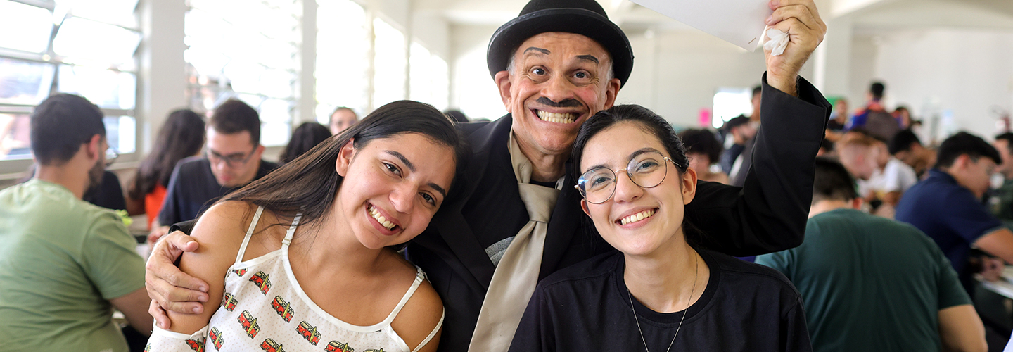 Duas alunas no Restaurante Universitário posam com ator durante almoço no Dia do Estudante